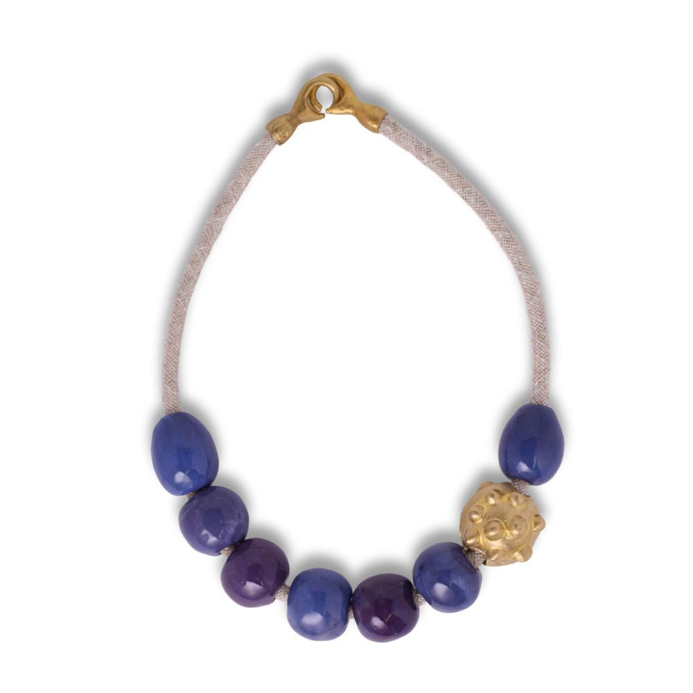 Una collana della collezione Archeperla realizzata a mano con perle tonde in ceramica color viola mirtillo e una forma a punte in ottone