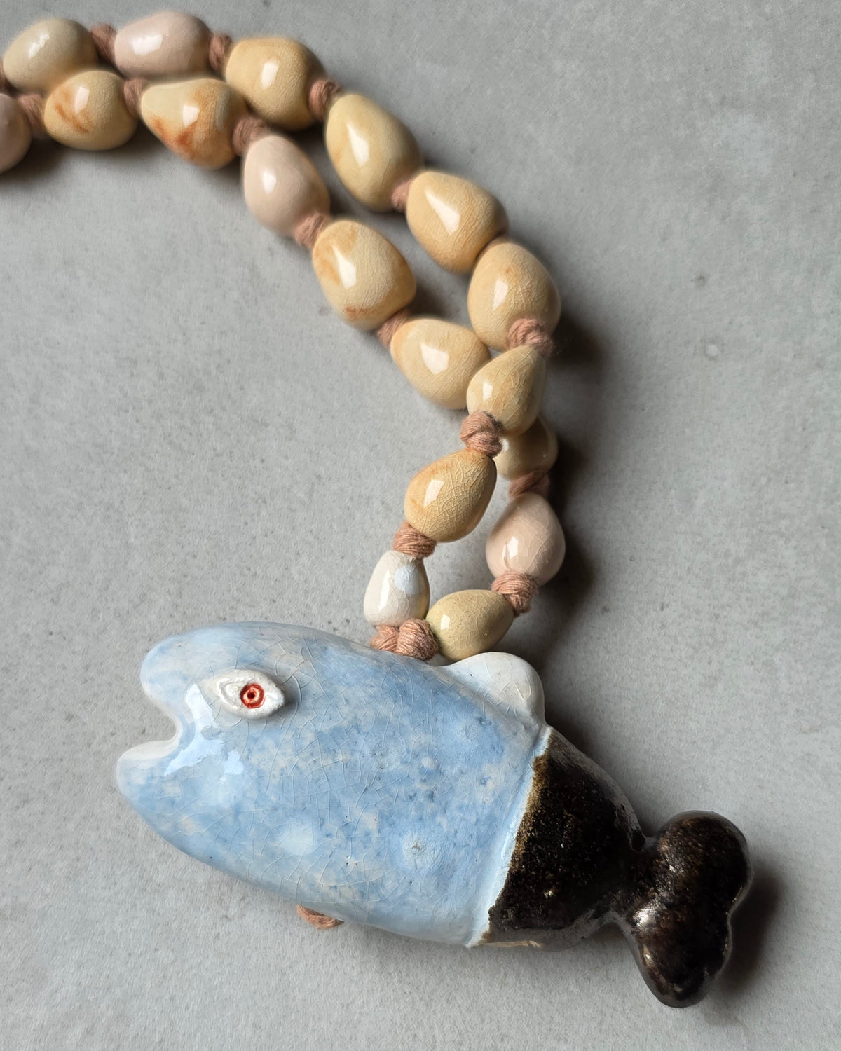 Collana Pesce Azzurro – il pesce da vicino, azzurro sfumato con pinna dorsale bianca e coda marrone scuro, sopra le perle sabbia e rosa