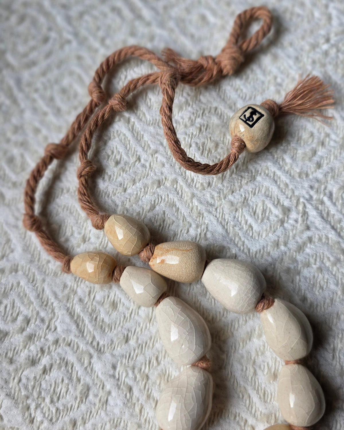 Collana Pesce Raro – la perla in ceramica firmata SF sulla corda di cotone rosata, accanto alle perle avorio e sabbia