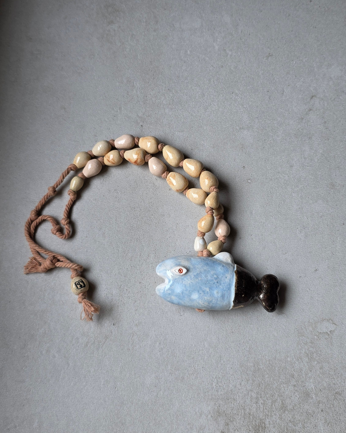 Collana Pesce Azzurro – il pesce rivolto a sinistra con la coda scura, e le perle sabbia e rosa ripiegate sopra
