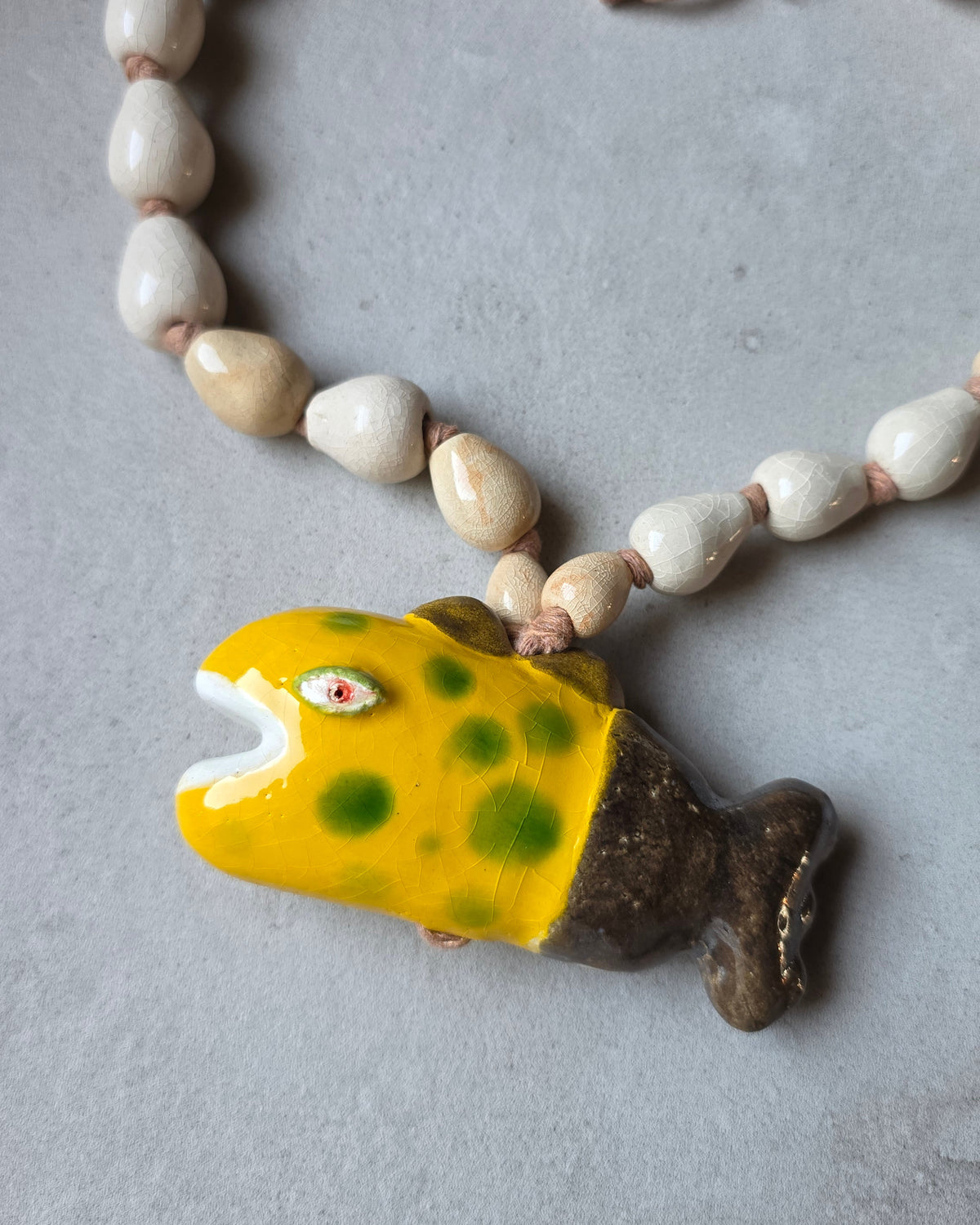 Collana Pesce Raro – dettaglio del pesce su fondo grigio, con le perle bianco avorio e sabbia sopra la pinna