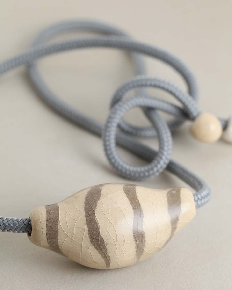 Una collana in ceramica che ricorda la forma di una conchiglia stilizzata, bianco avorio con disegni grigio sabbia