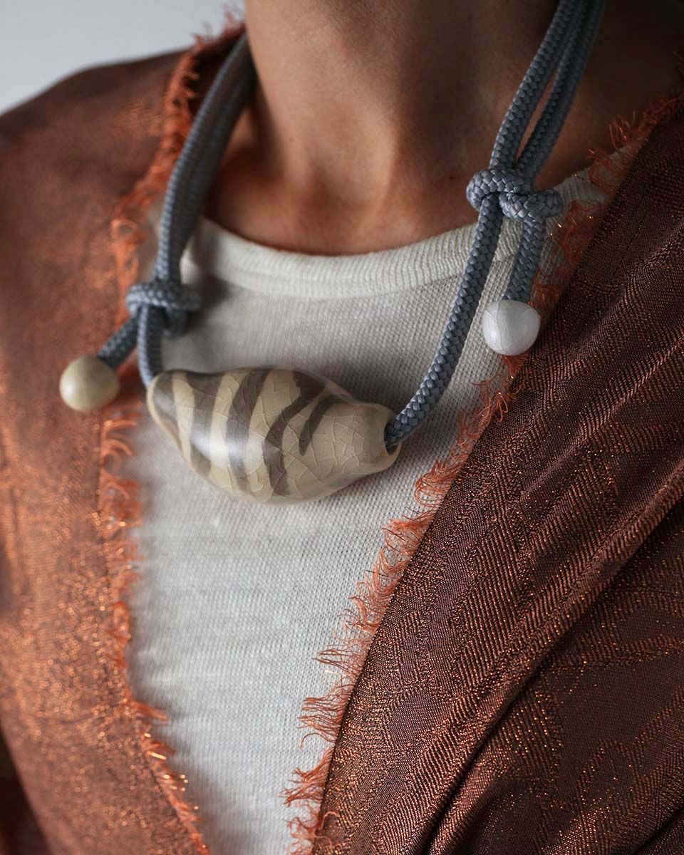 Una collana in ceramica che ricorda la forma di una conchiglia stilizzata, bianco avorio con disegni grigio sabbia