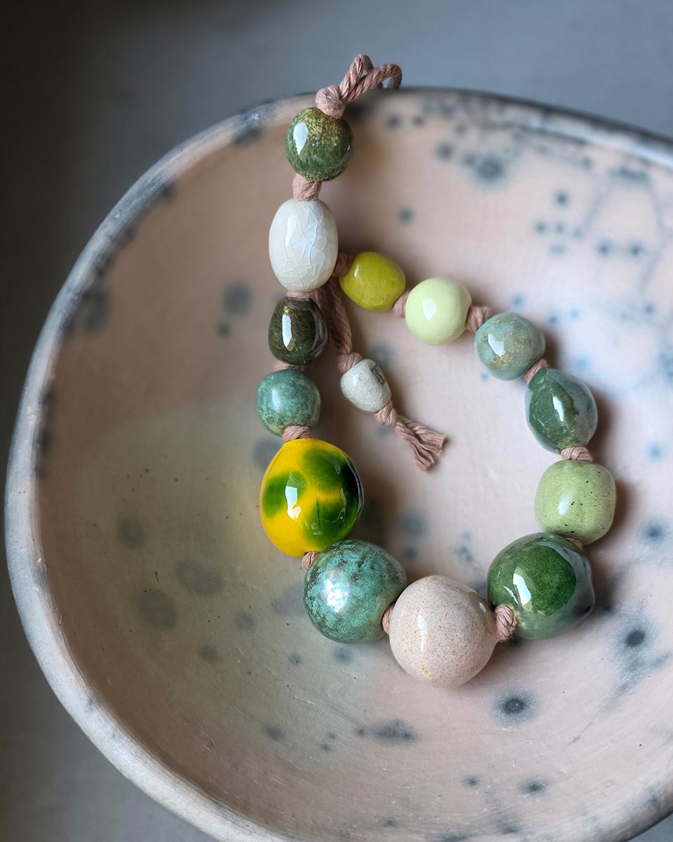 una collana artigianale in ceramica dalle perle brillanti appoggiata in una ciotola in ceramica raku dalla finitura satinata