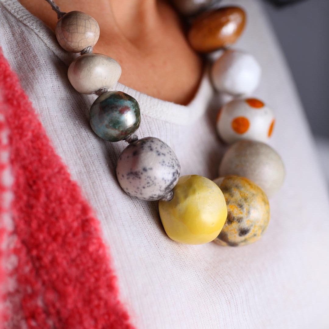 Donna con cardigan rosso indossa una collana di grandi perle in ceramica bianche, gialle, marroni, a pois arancioni e grigio blu