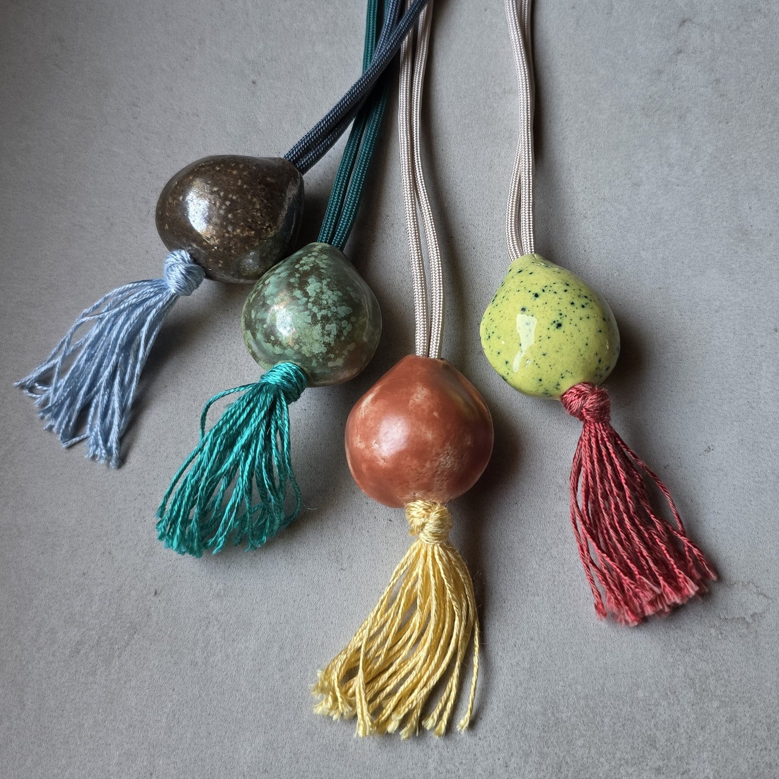 Le quattro collane Sacro Om una accanto all'altra: perle oro, turchese, terracotta e gialla, con nappine azzurra, verde, gialla e rossa