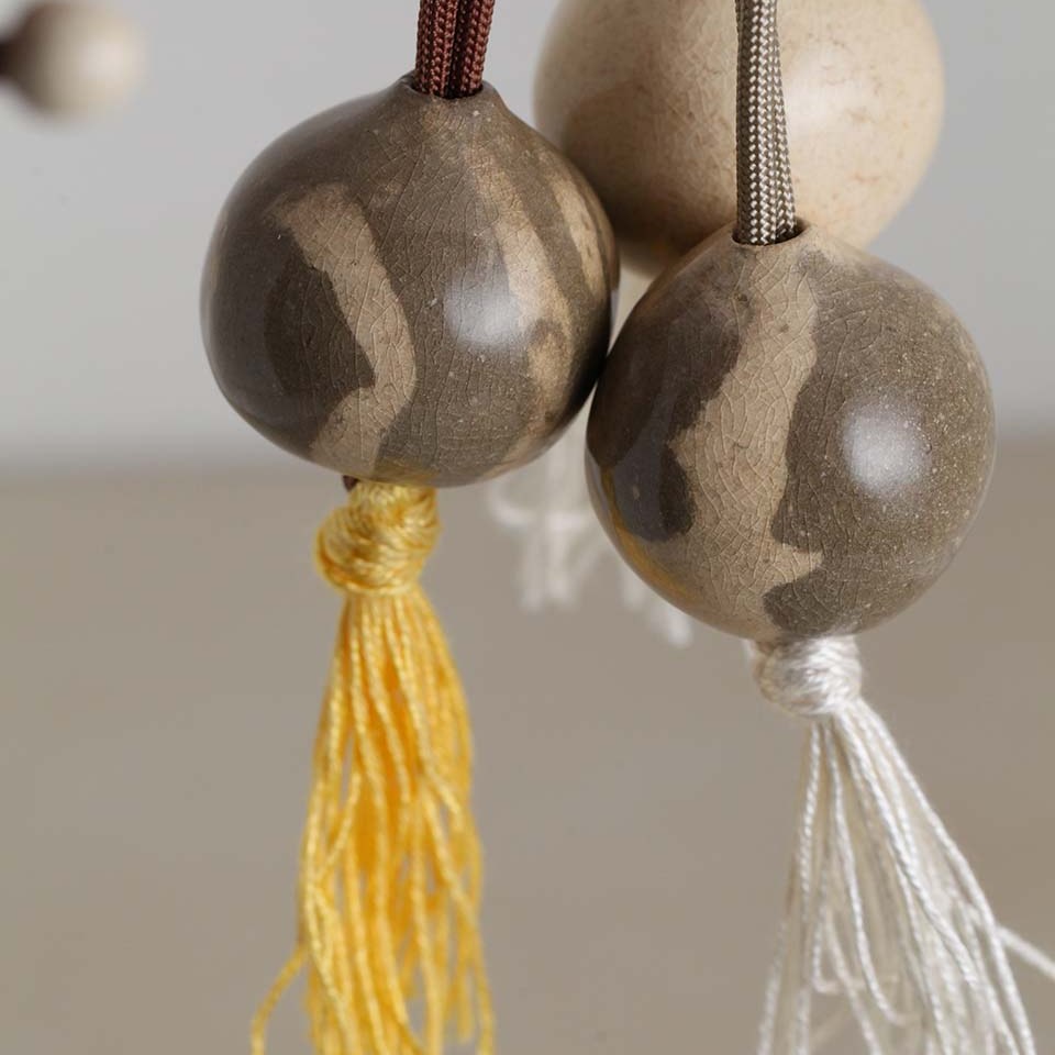 Tre perle nomadi in ceramica grigio sabbia con nappine gialla e avorio, appese a cordini marrone e tortora